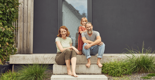 Eine Famile sitzt auf der Treppe vor ihrem neuen Haus