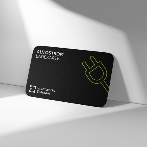Man sieht die Ladekarte an eine Wand angelehnt. Die Ladekarte der Stadtwerke ist schwarz und in weiß ist oben in der linken Ecke Autostrom Ladekarte geschrieben. Unten in der linken Ecke sieht man das Stadtwerke Logo und leckts einen grünen Stecker.