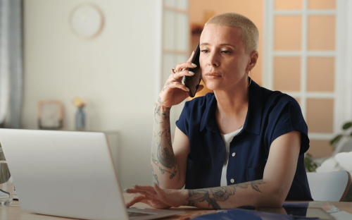 Eine Frau sitzt vor einem Laptop und telefoniert.