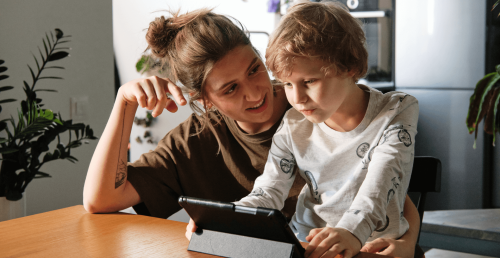 Frau und Kind sitzen gemeinsam am Tisch und schauen auf ein Tablet – modernes Familienleben mit digitaler Vernetzung.