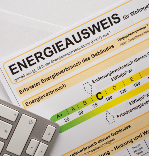 Nahaufnahme eines Energieausweises mit Farbskala zur Effizienzklasse und Tastatur-Ausschnitt.