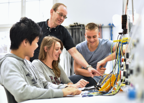 Ausbilder erklärt einer Gruppe junger Menschen ein elektrisches Messgerät in der technischen Ausbildung.
